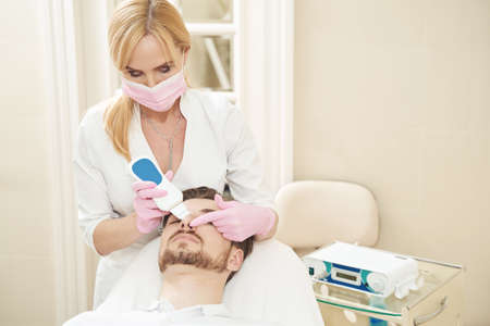 Woman beauty worker processing man nose with ultrasonic skin scrubber