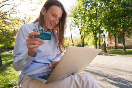 Cheerful woman doing online payments in park
