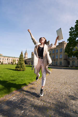 Woman with laptop jumping with joy outdoor