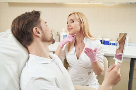Cosmetologist showing patient place on neck for beauty procedure