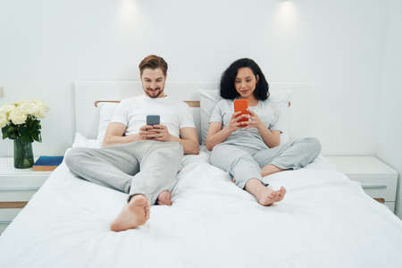 Young family couple with cellphones in bedroomの写真素材
