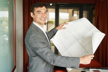 Pleased project manager holding building layout and smilingの写真素材