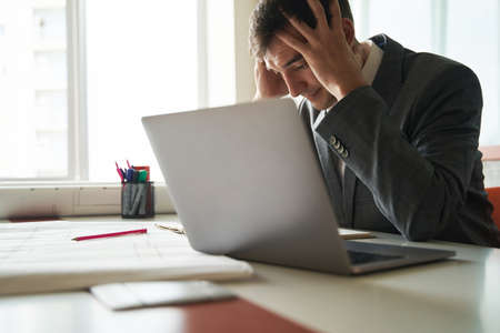 Stressed worker grabbing his head during work on laptopの写真素材
