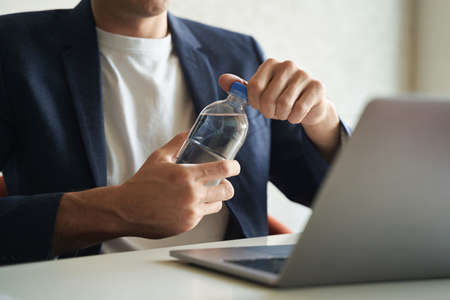 Worker opening bottle of water in front of laptopの写真素材