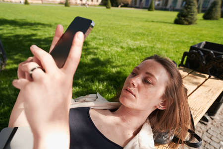 Lady is using a mobile gadget on a park bench