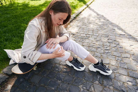 Lady is writhing in pain in leg sitting on skateboardの写真素材