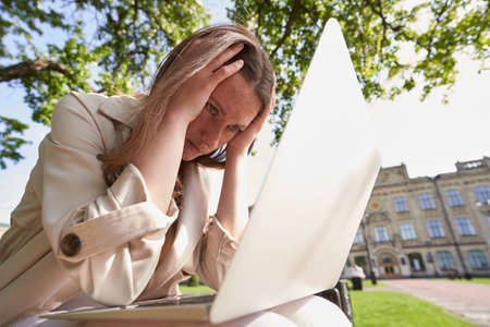 Lady holding her hands on head on bench in park