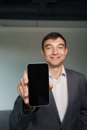 Joyful man introducing smartphone to camera with smileの写真素材