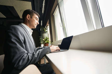 Business worker typing on laptop at window deskの写真素材