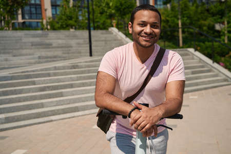 Joyous young man with e-scooter standing on pavement