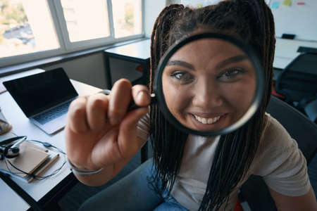 Joyous female office worker looking at something through loupeの写真素材