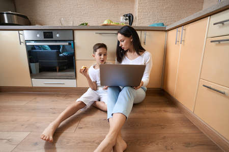 Mother and son sitting with laptop on the floorの写真素材