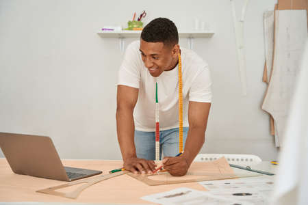 Jolly fashion designer using laptop in atelier