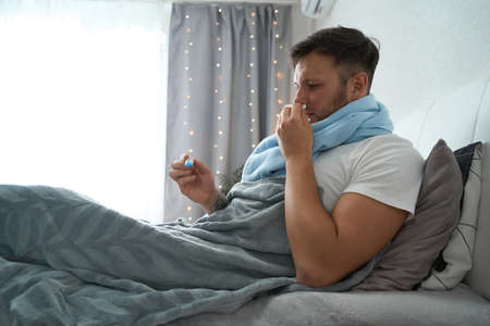 Guy lies in bed with a runny nose and feverの写真素材