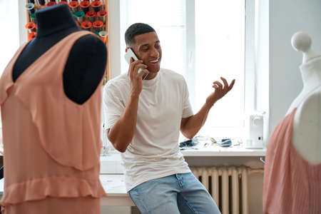Jolly man speaking on smartphone in dressmaker shopの写真素材
