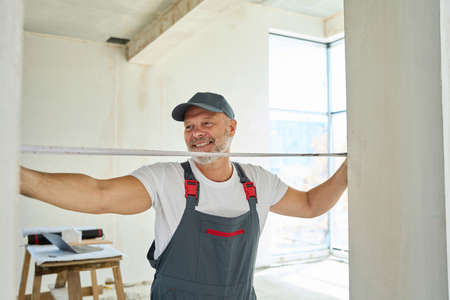 Smiling gray-haired worker measures width of doorway with tape measureの写真素材