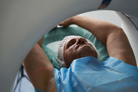 Patient his eyes closed and arms outstretched lies in tomography chamberの写真素材