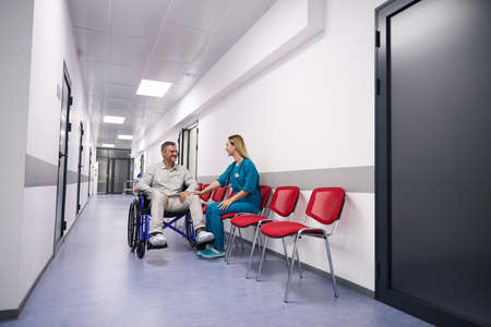 Man in wheelchair communicates with female doctor in corridor outpatient clinicの写真素材