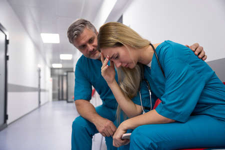 Two sad doctors are sitting in the corridor of hospitalの写真素材