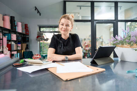 Cute florist sits at table of floral store and smilesの写真素材