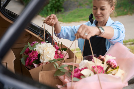 Florist puts packages with bouquets of flowers in car trunkの写真素材