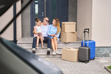 Mother, father and daughter are sitting on steps new homeの写真素材