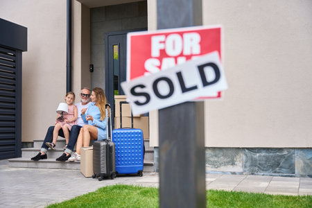 Father, daughter and mother sit on threshold. Sign for saleの写真素材