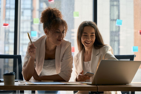 Women colleagues communicate with each other and look at laptopの写真素材