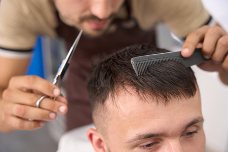Committed barbershop worker being busy combing and cutting hairの写真素材