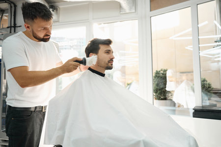 Professional barber sweeping pieces of shaved hair off of clientの写真素材