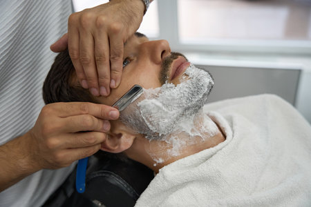 Careful barber using straight razor to shave man faceの写真素材