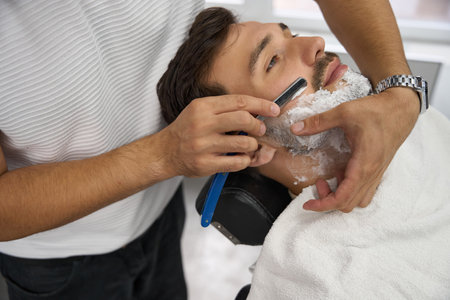 Handsome man enjoying the face shave by a professional barberの写真素材