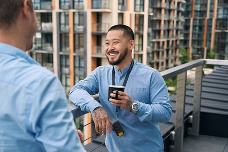 Cheerful corporate worker and his coworker talking on balcony