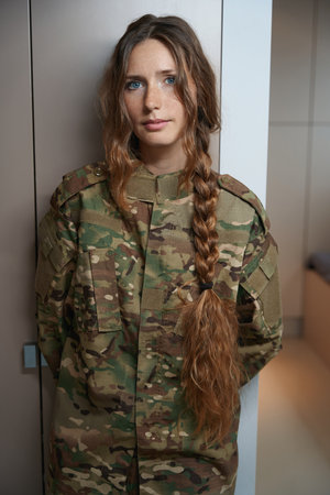 Woman in a camouflage uniform stands by closet in roomの写真素材