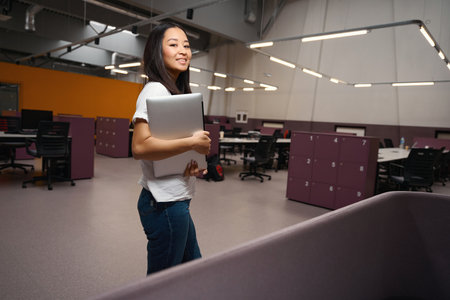 Elegant pretty female with computer is standing in the open space workplace