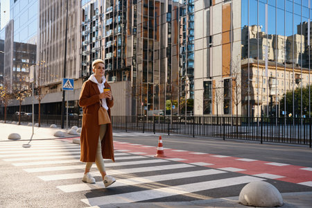 Stylish woman in a wool coat walks along a crosswalkの写真素材