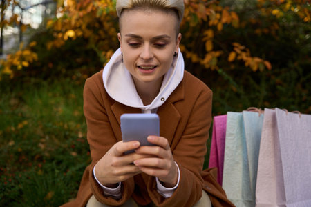 Blonde female in coat is resting after shopping in autumn park