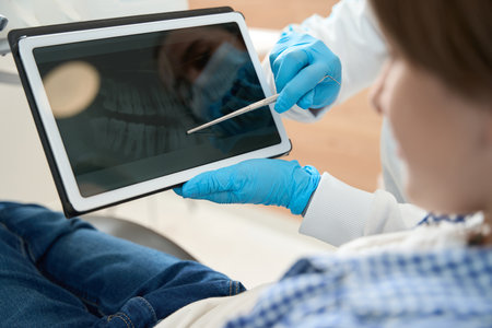 Dentist showing dental image on clipboard to young patientの写真素材