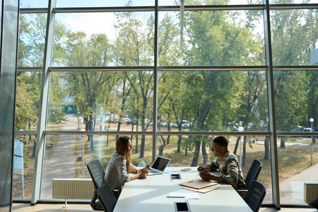 Two colleagues with coffee sitting on the table and talking in the office