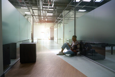 African American man sitting on the floor and typing a message on the phoneの写真素材