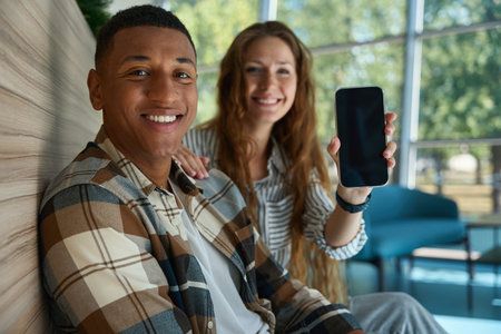 Pretty woman holding phone and sitting next to her male colleague