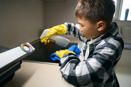 Teenager gently sprays detergent on a kitchen stoveの写真素材