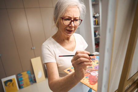 Talented elderly lady paints a picture in a bright roomの写真素材