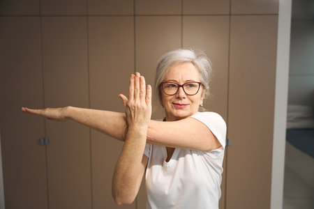 Pleasant grandmother in glasses is standing in an asanaの写真素材