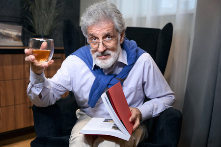 Lonely grandfather sits in chair with book and a drinkの写真素材