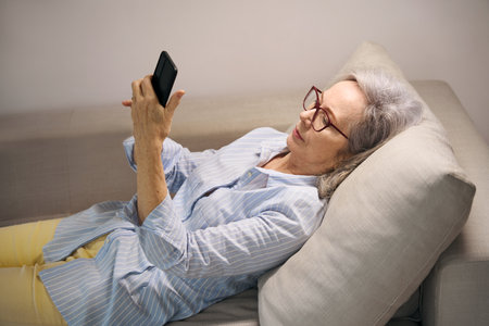Elderly woman resting home looks at something on her phone