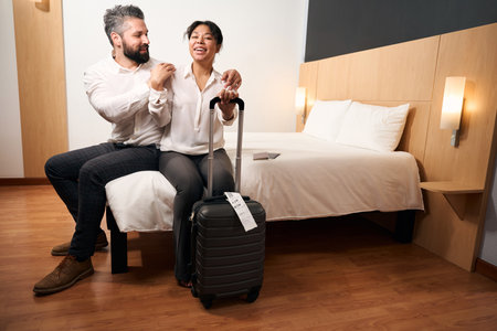 Romantic tourist couple with luggage seated in hotel roomの写真素材