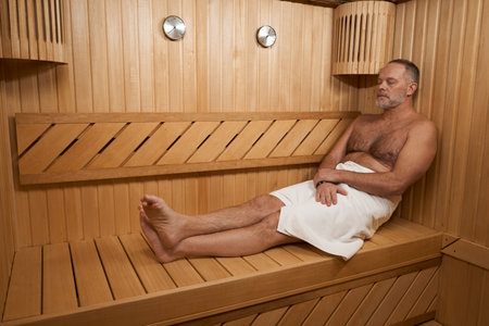 Middle-aged man with naked torso is warming himself in saunaの写真素材