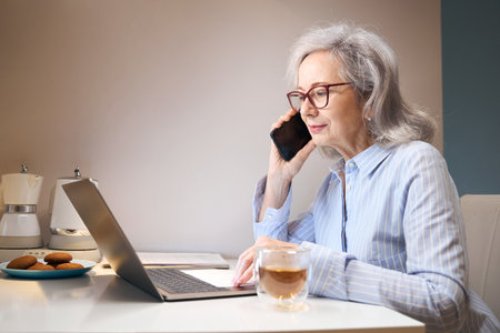 Active elderly lady works from home, she communicates on phone
