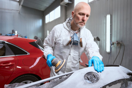 Man in overalls works with an unpainted car bumper